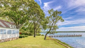 A house with a stone foundation, a grassy yard, and a dock extending into a lake. - Shelter Island remodeled 1937 Cape Cod Waterfront with Deepwater Dock (Shelter Island)