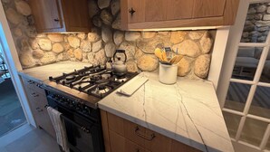 A kitchen with a gas stove, a kettle, and a stone wall backsplash. - Shelter Island remodeled 1937 Cape Cod Waterfront with Deepwater Dock (Shelter Island)
