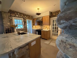 A kitchen with a stone wall, wooden cabinets, a marble countertop, and a built-in stove.