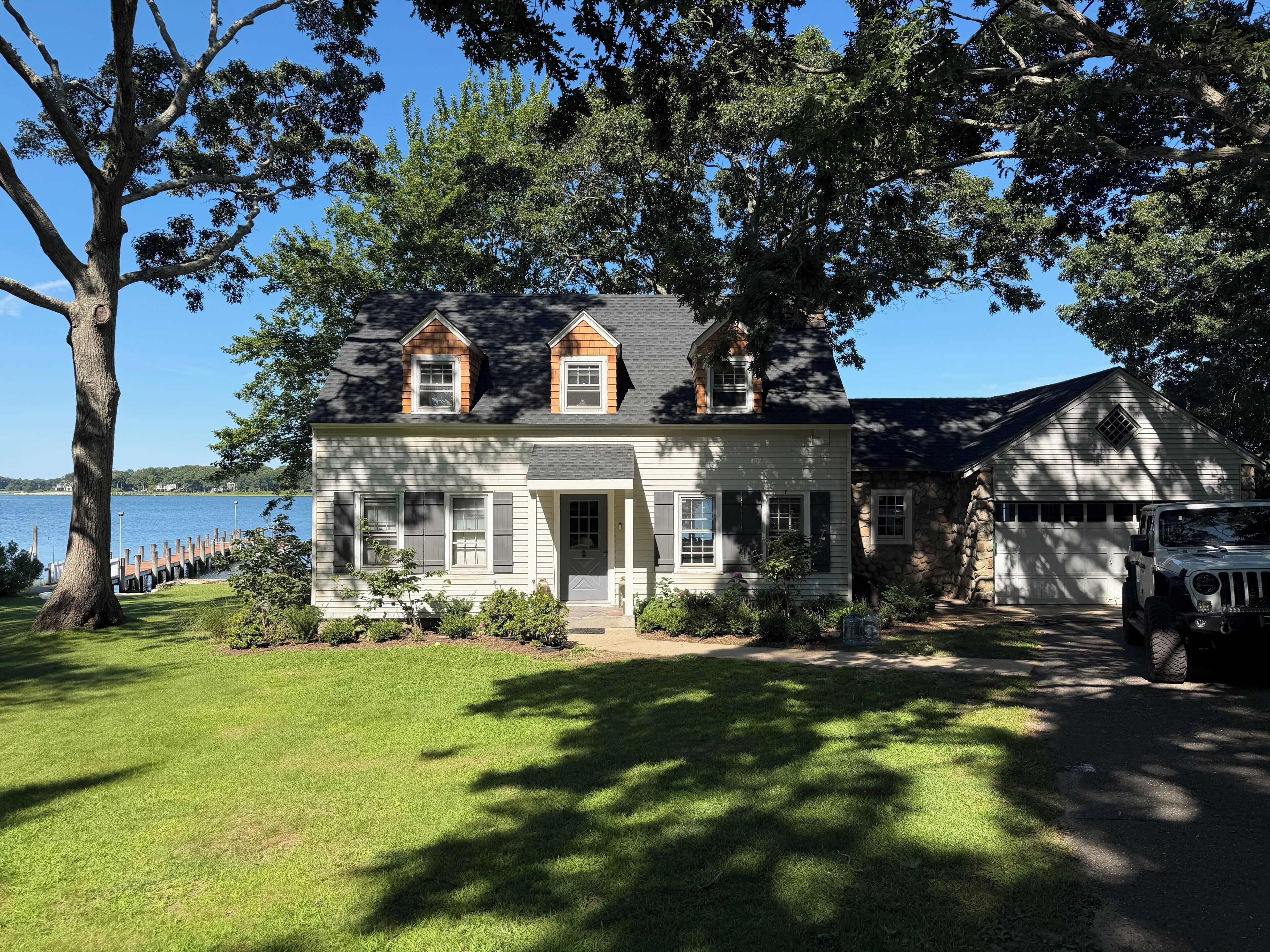 A two-story house with a garage, a lawn, and a dock extending into a body of water.