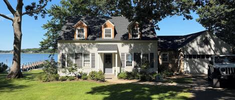 A two-story house with a garage, a lawn, and a dock extending into a body of water.