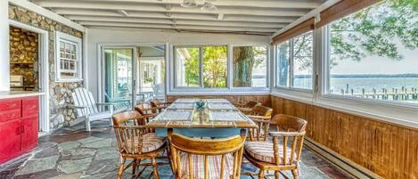 A covered dining area with a large table and chairs, stone walls, and a view of the water.
