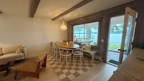 A dining area with a round table and chairs, a sofa, and a view of a lake through large windows. - Shelter Island remodeled 1937 Cape Cod Waterfront with Deepwater Dock (Shelter Island)