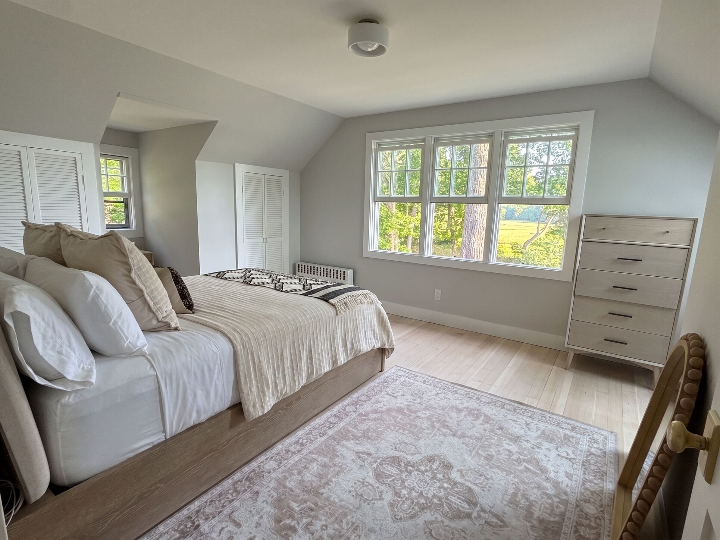 Un dormitorio con cama, cómoda, radiador y ventana con vistas a la vegetación.