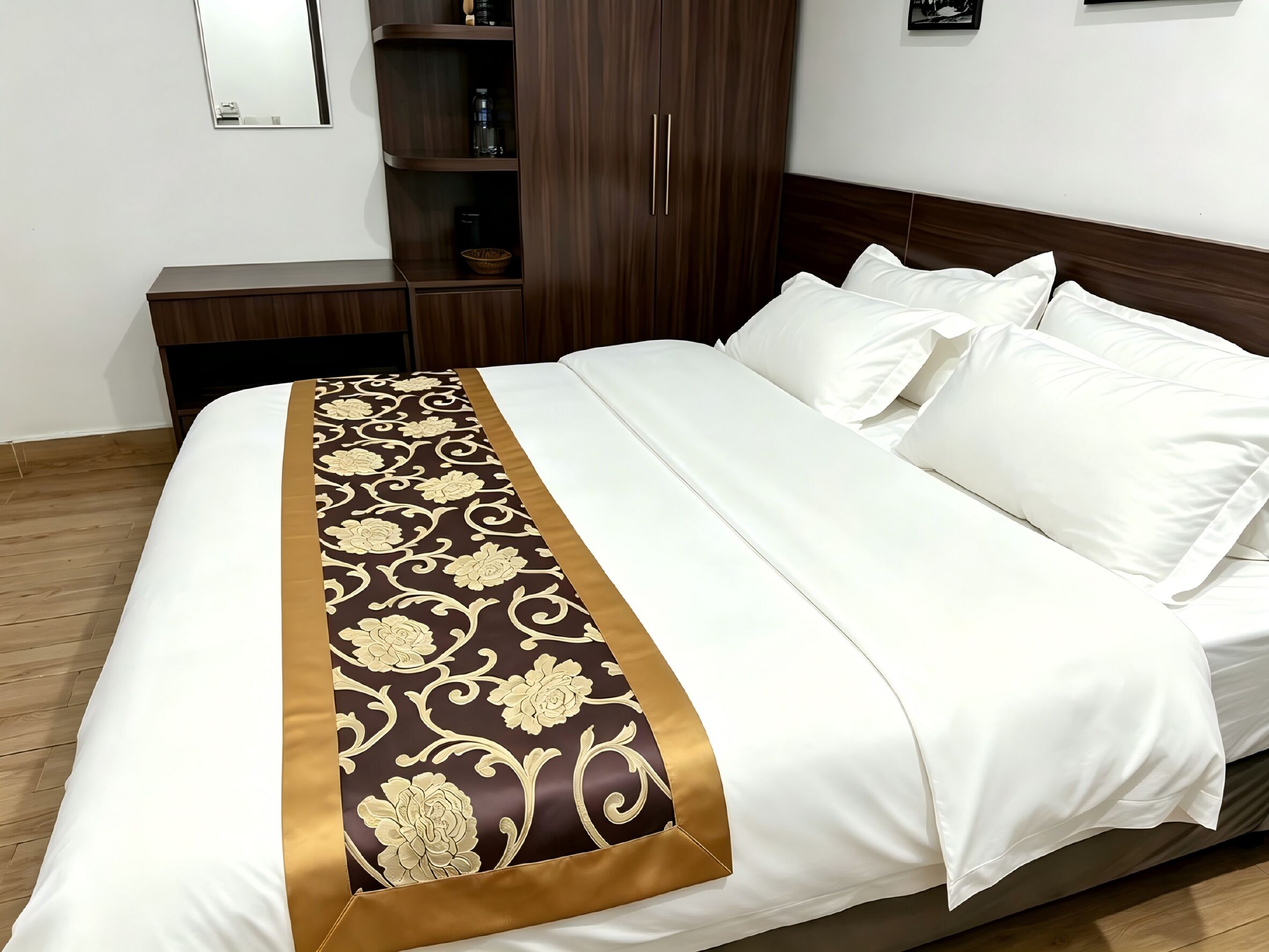 A neatly made bed with white linens and a decorative gold and brown bed runner.
