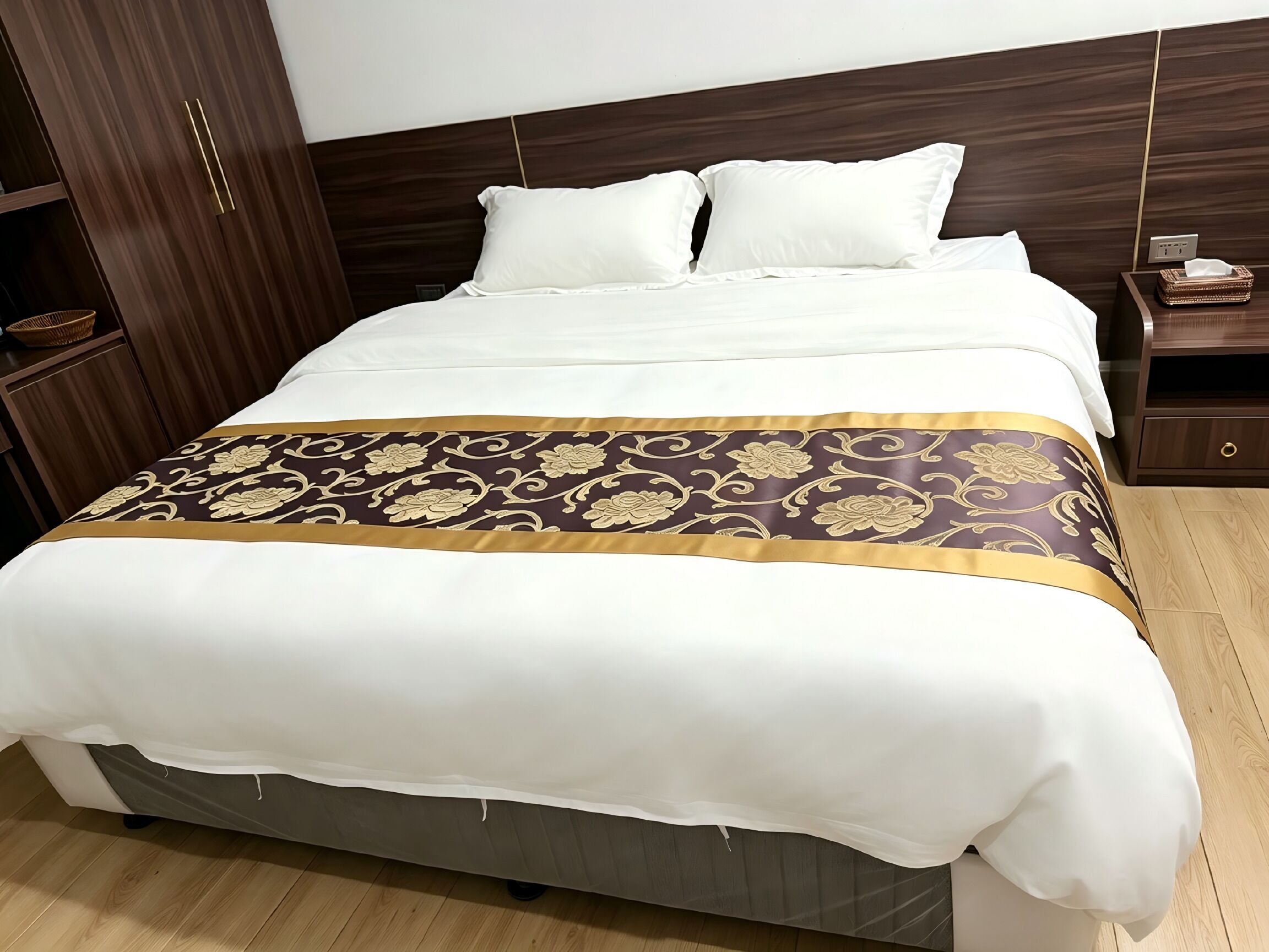Un lit bien fait, avec une couette blanche et un couvre-lit décoratif aux motifs dorés et bruns.