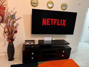 A modern living room with a flat-screen TV displaying 'NETFLIX' in red letters, a decorative vase with flowers, and a black entertainment unit with drawers. - Jevico Villa - Near Ocho Rios - Starlink - Solar - Gated (Priory)