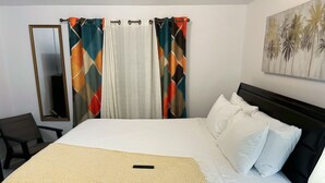 Hotellihuone, jossa on sänky, tuoli, peili ja taulu seinällä.
