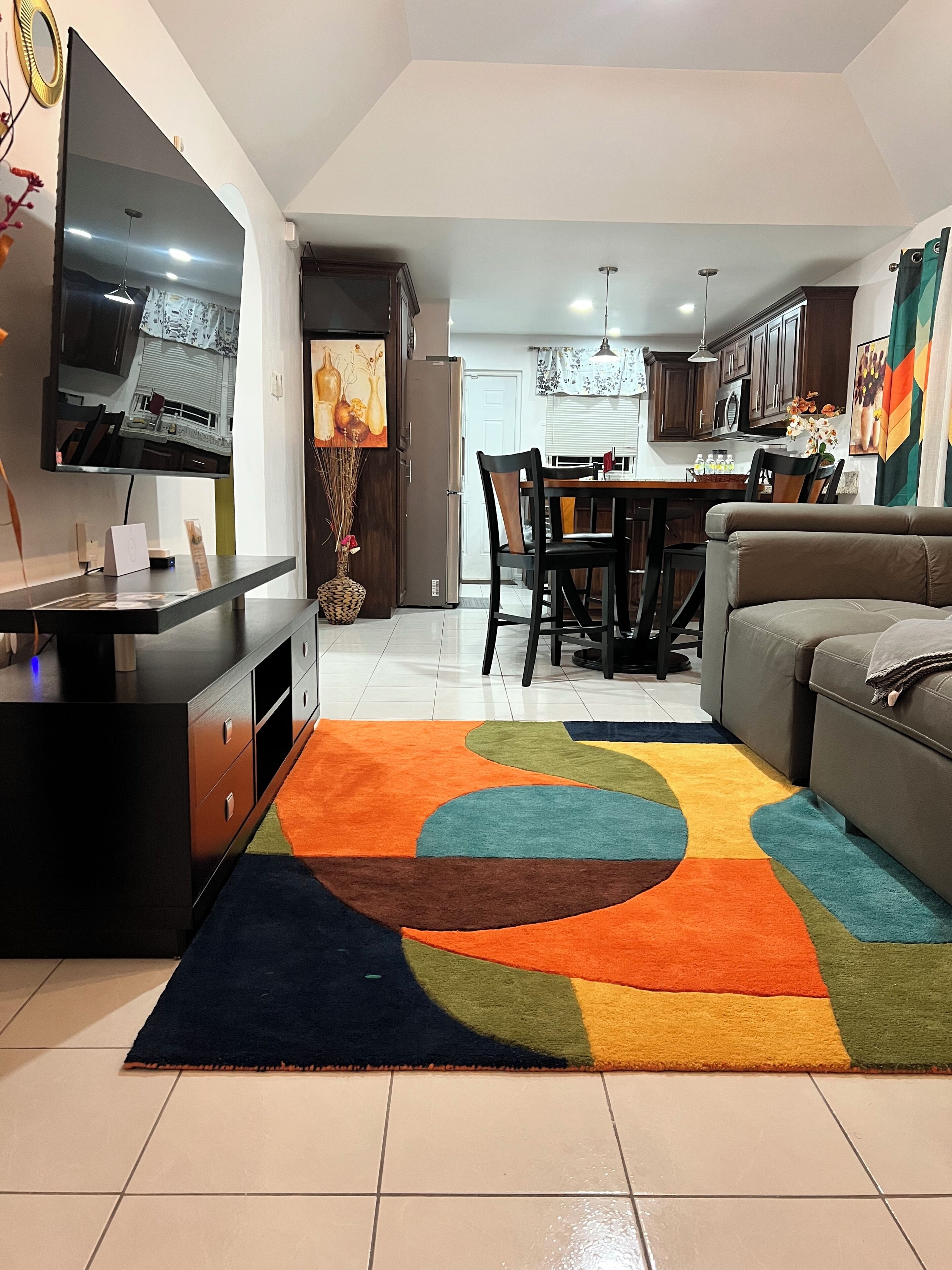 Ein modernes Wohnzimmer mit Fernseher, Sofa und einem farbenfrohen Teppich.
