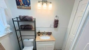 A compact bathroom with a toilet, a sink, and a shelf with towels. - Modern EaDo Home Near Downtown, Stadiums, Medical Center & Top Houston Attractions (Houston)