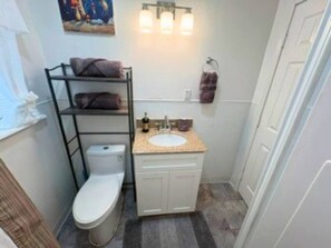 A compact bathroom with a toilet, a sink, and a shelf with towels. - Modern EaDo Home Near Downtown, Stadiums, Medical Center & Top Houston Attractions (Houston)
