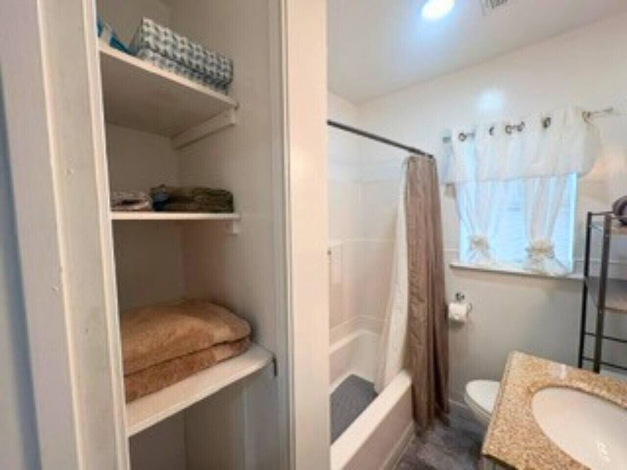 A bathroom with a shower, toilet, and a shelf with towels.