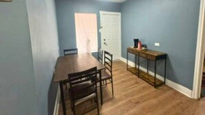 A dining area with a wooden table and chairs, a small side table, and a door in the background. - Modern EaDo Home Near Downtown, Stadiums, Medical Center & Top Houston Attractions (Houston)