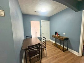 A dining area with a wooden table and chairs, a small side table, and a door in the background. - Modern EaDo Home Near Downtown, Stadiums, Medical Center & Top Houston Attractions (Houston)