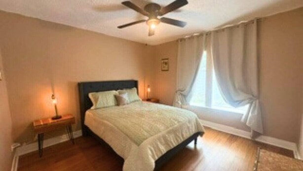 A bedroom with a bed, bedside tables, a ceiling fan, and a window with curtains. - Modern EaDo Home Near Downtown, Stadiums, Medical Center & Top Houston Attractions (Houston)