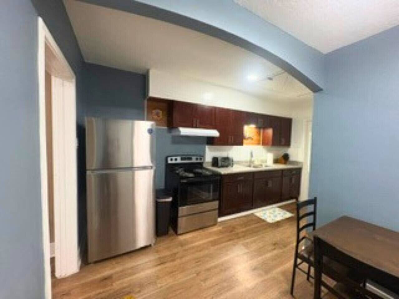 A compact kitchen with a refrigerator, stove, and microwave, wooden cabinets, and a dining table with chairs.