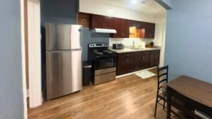 A compact kitchen with a refrigerator, stove, and microwave, wooden cabinets, and a dining table with chairs. - Modern EaDo Home Near Downtown, Stadiums, Medical Center & Top Houston Attractions (Houston)