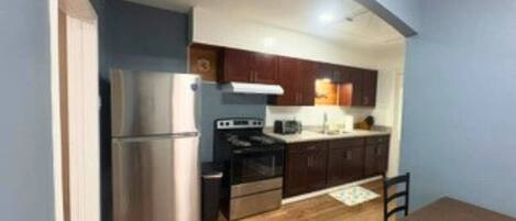 A compact kitchen with a refrigerator, stove, and microwave, wooden cabinets, and a dining table with chairs.