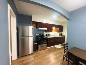 A compact kitchen with a refrigerator, stove, and microwave, wooden cabinets, and a dining table with chairs. - Modern EaDo Home Near Downtown, Stadiums, Medical Center & Top Houston Attractions (Houston)