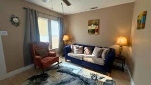 A living room with a blue sofa, a red armchair, a ceiling fan, and a rug. - Modern EaDo Home Near Downtown, Stadiums, Medical Center & Top Houston Attractions (Houston)
