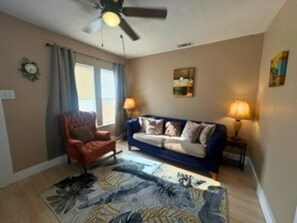 A living room with a blue sofa, a red armchair, a ceiling fan, and a rug. - Modern EaDo Home Near Downtown, Stadiums, Medical Center & Top Houston Attractions (Houston)