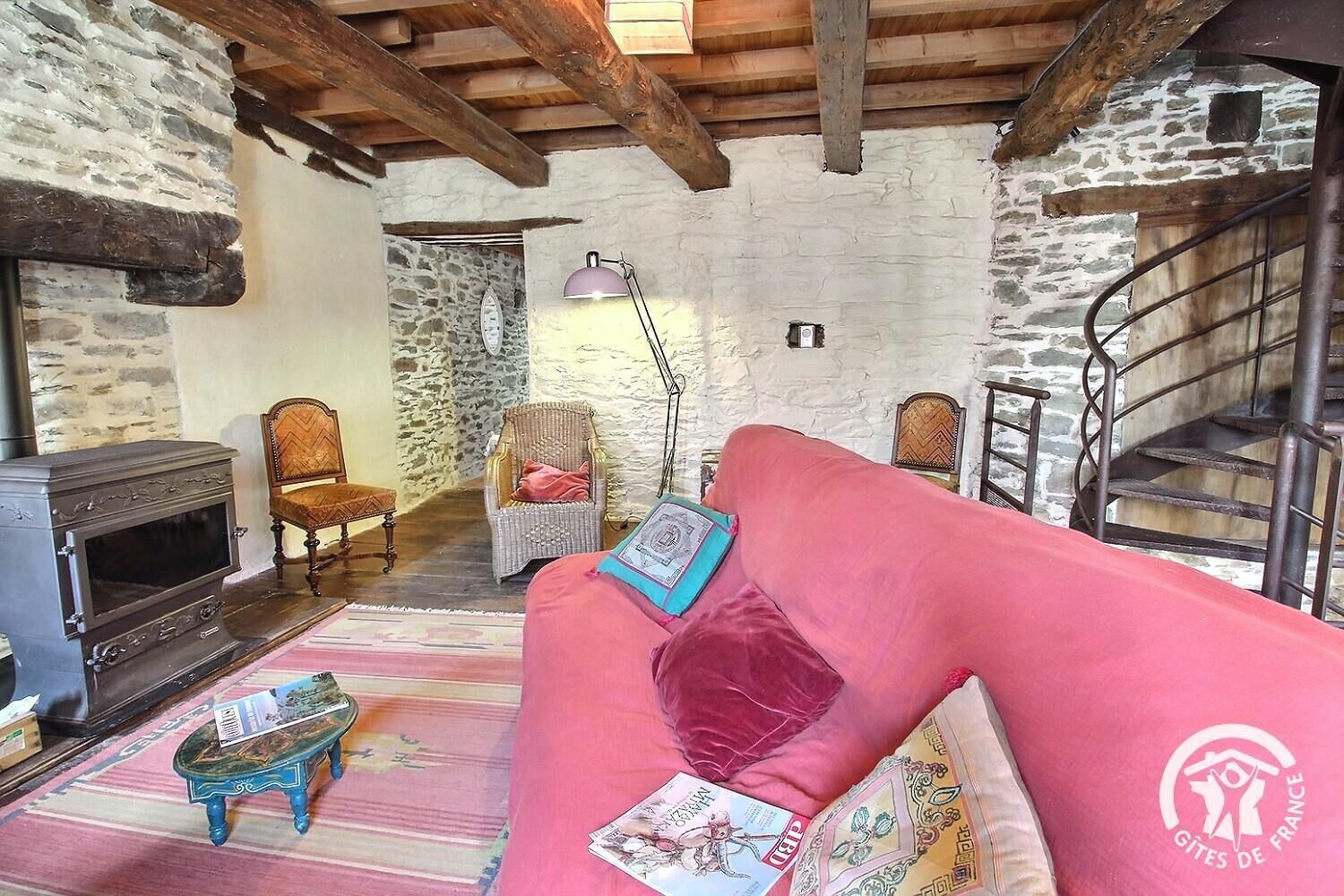 A rustic room with a stone wall, wooden beams, a fireplace, a pink sofa, and a staircase.