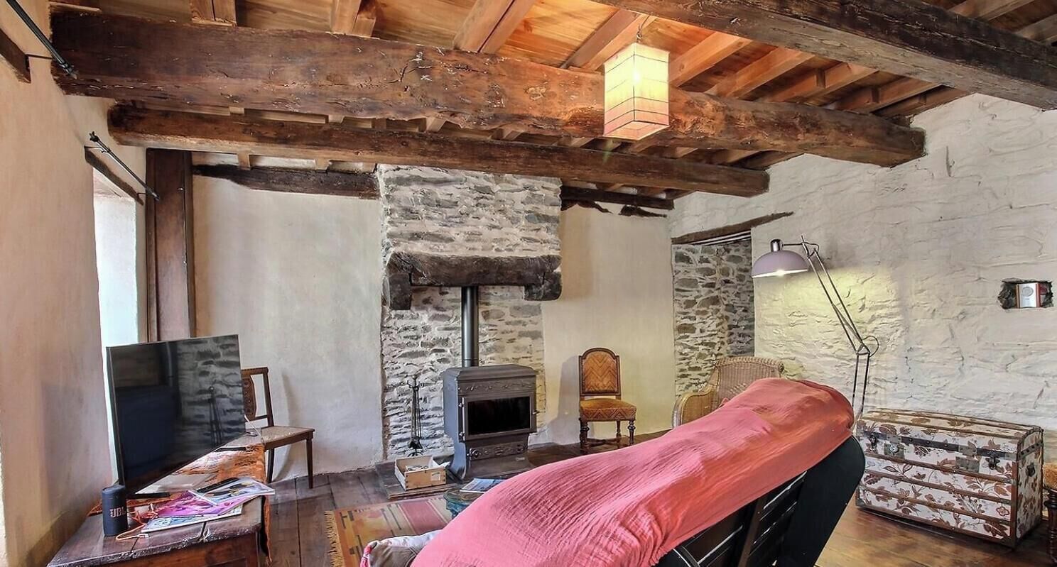 A rustic room with exposed wooden beams, a stone wall, a fireplace, a bed, a television, and a suitcase.