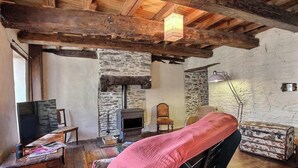 Ein rustikaler Raum mit freiliegenden Holzbalken, einer Steinwand, einem Kamin, einem Bett, einem Fernseher und einem Koffer.