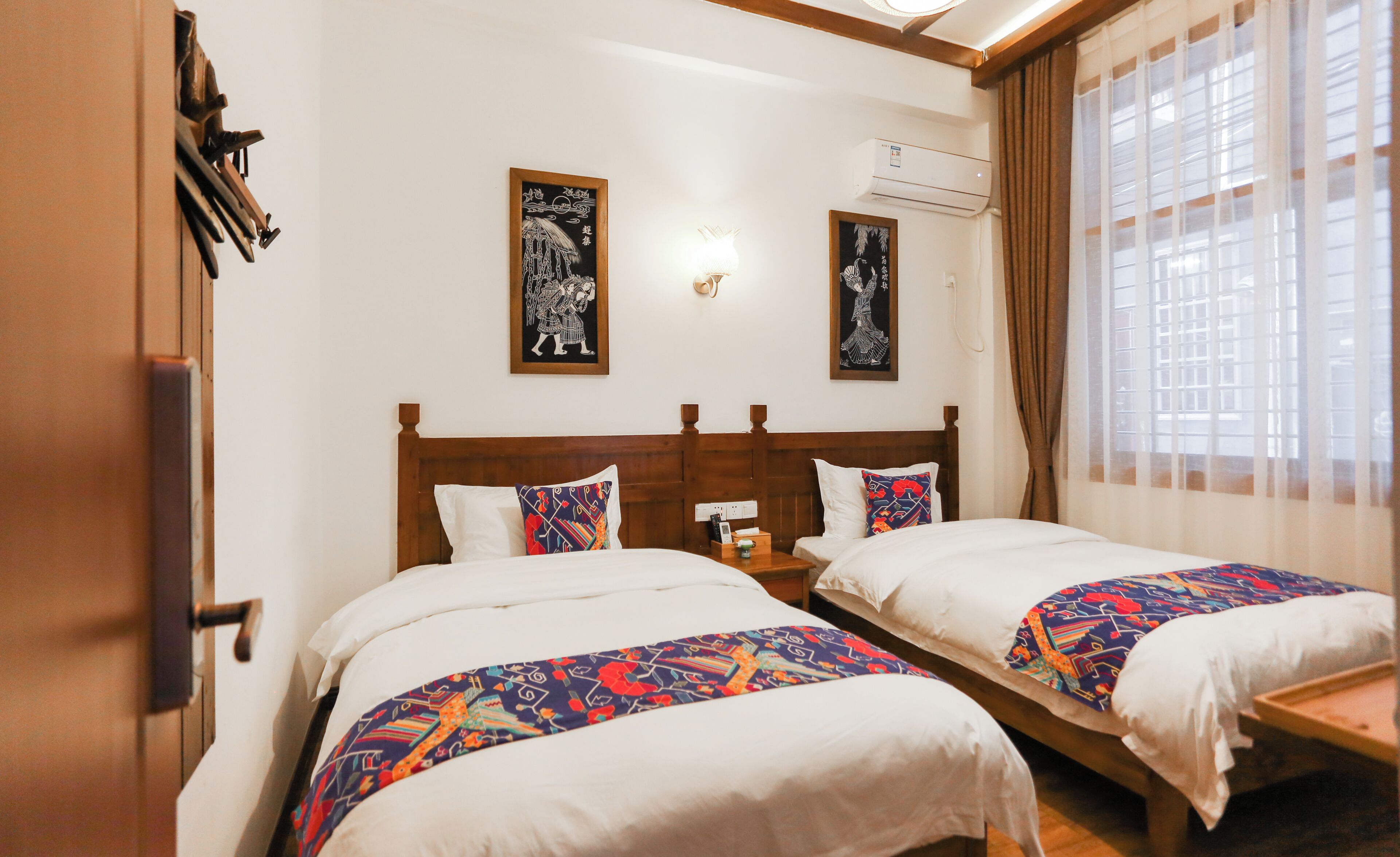 Habitació d'hotel amb dos llits, un capçal de llit de fusta, aire condicionat fixat a la paret i una finestra amb cortines.