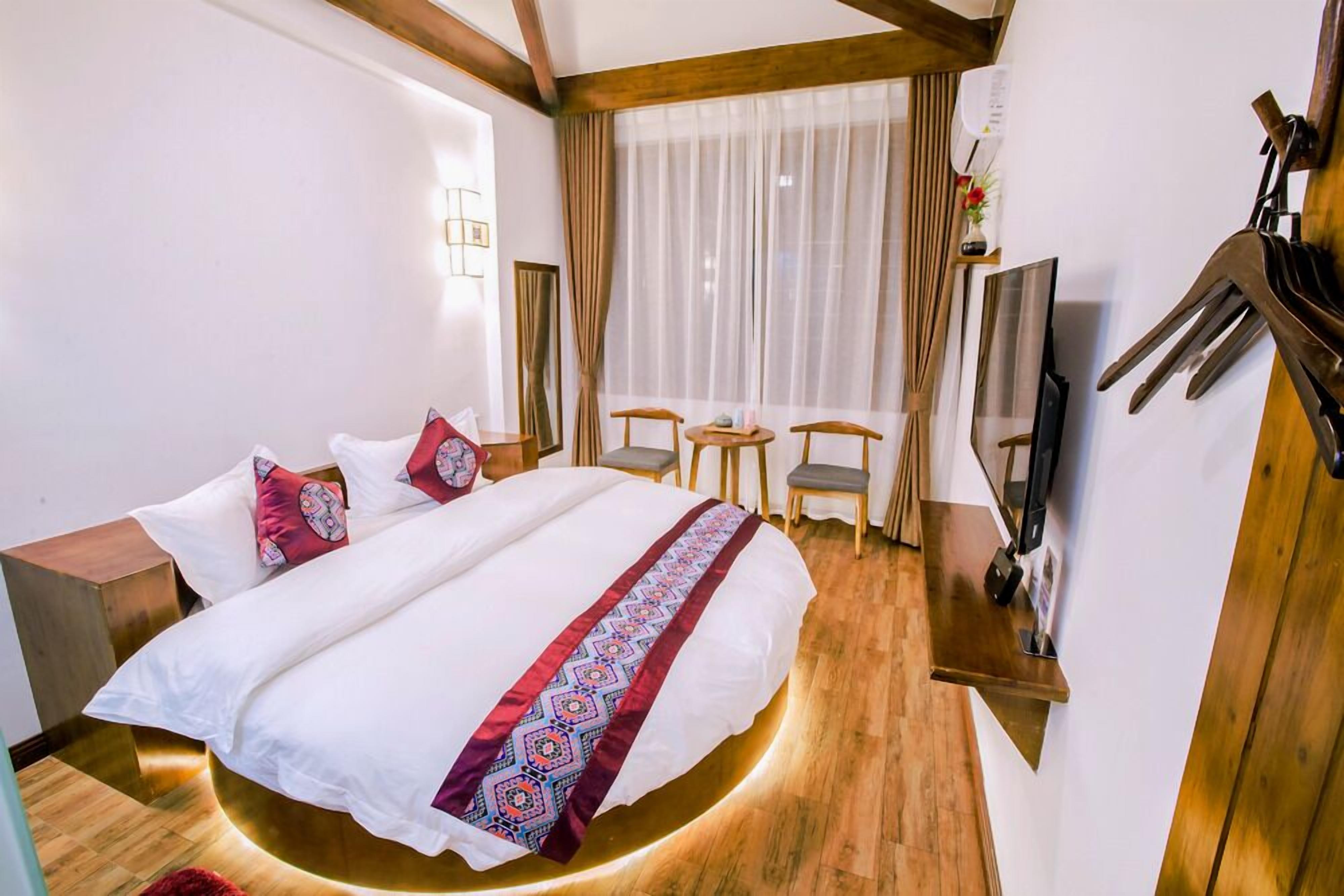A hotel room with a bed, a desk, a chair, a TV, and a window with curtains.