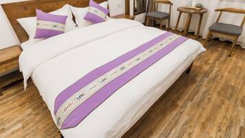 Un lit bien fait, avec une couvre-lit violette et blanche, une tête de lit en bois et un plancher en bois.
