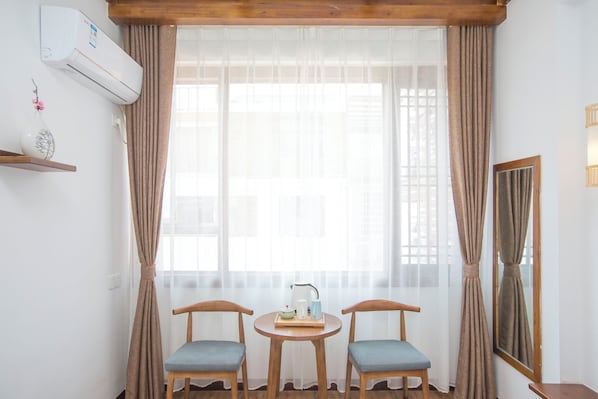 A room with two wooden chairs, a small round table with a kettle, a vase with flowers, and an air conditioning unit on the wall. - zhangjiaije hexi inn (Zhangjiajie)