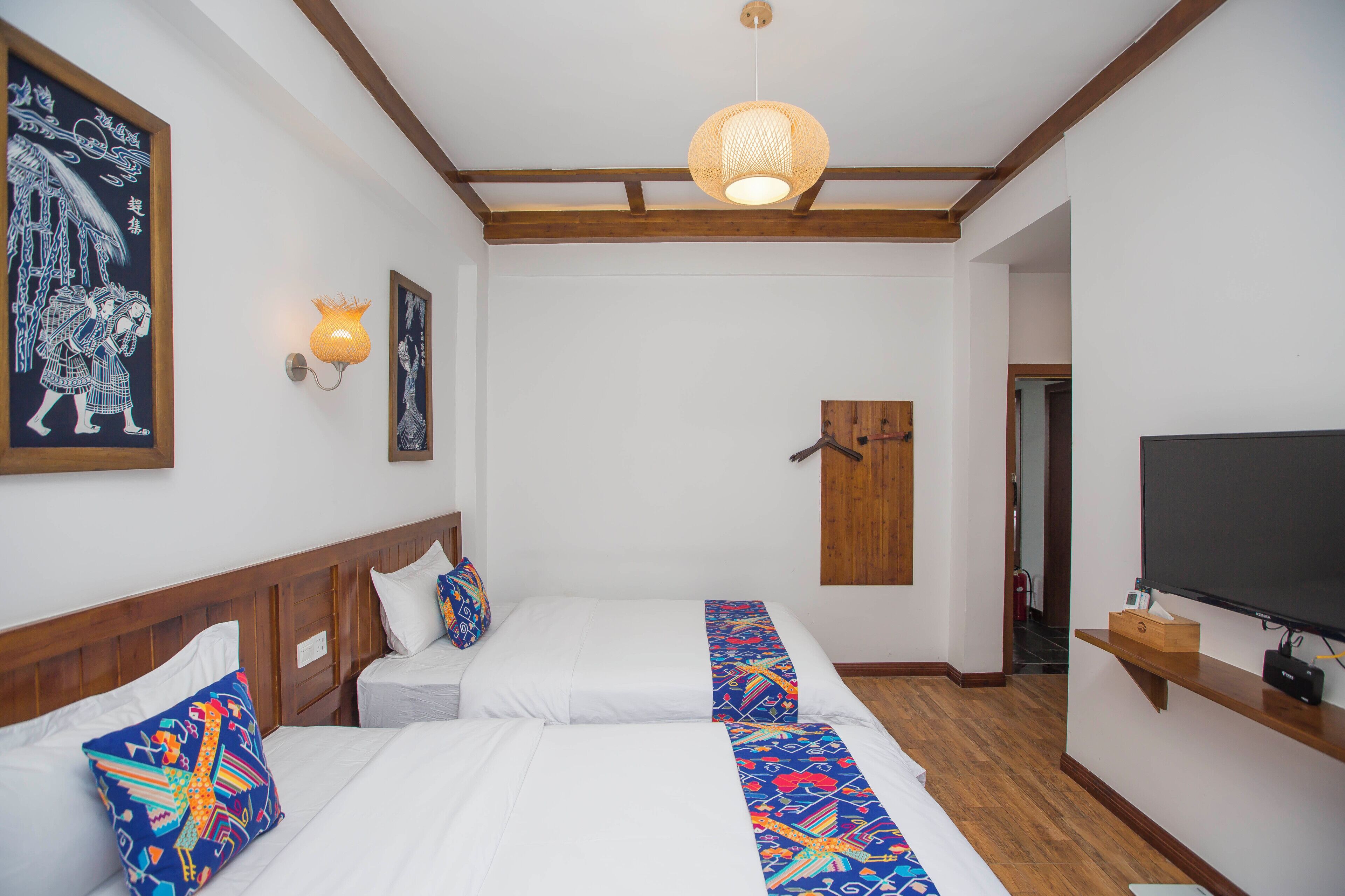 Quarto de hotel com duas camas, uma televisão, uma porta de madeira e um candeeiro no teto.