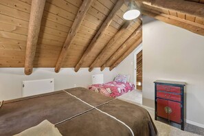 Een slaapkamer met een schuine wand, een bed met een beddegoed met een patroon, een dressoir en een deur naar een andere kamer.