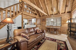 A log cabin interior with a leather sofa, dining table, and kitchen area. - Forest Hideaway Near Sedona | Log + Fire Pit (Munds Park)