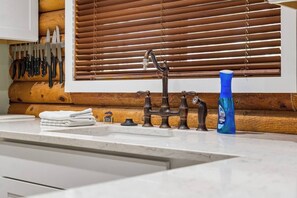 Eine Küche mit Holzrückwand, einem Spülbecken mit einem alten Wasserhahn und einer blauen Flasche Geschirrspülmittel.