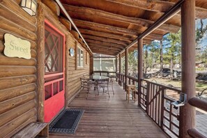 Eine Holzhütte mit verdeckter Veranda, einem Esstisch mit Stühlen und einem Schild mit der Aufschrift 'Home Sweet Home'.