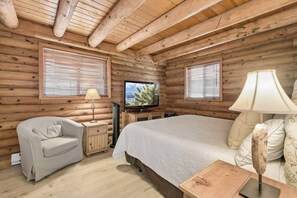 A log cabin room with a bed, a television, a chair, and a lamp. - Forest Hideaway Near Sedona | Log + Fire Pit (Munds Park)