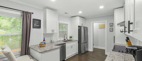 Cocina moderna con armarios blancos, un refrigerador de acero inoxidable y una encimera de granito.