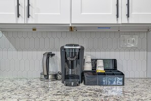 Une cuisine équipée d’une machine à café, d’un distributeur d’eau et d’un support à capsules de café sur le plan de travail.