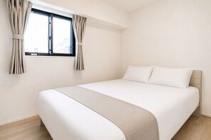 Uma cama de solteiro com cabeceira, uma janela com cortinas e chão de madeira.