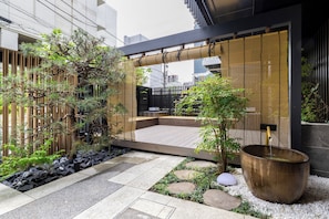 Un espacio exterior moderno con una terraza de madera, una fuente grande y varias plantas.