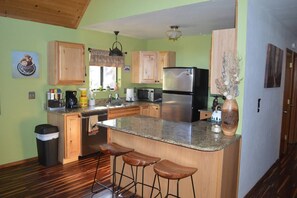 A kitchen with wooden cabinets, a stainless steel refrigerator, a microwave, and a coffee maker. There are three wooden stools at the island. - Incredible Whispering Pines Escape (Pinetop Country Club)