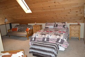 A cozy attic bedroom with a sloped ceiling, a bed with patterned bedding, a chair with a fur throw, and a dresser. - Incredible Whispering Pines Escape (Pinetop Country Club)