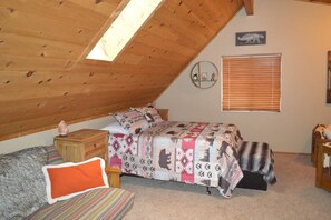 A bedroom with a sloped ceiling, a bed with patterned bedding, a wooden nightstand, a small table with a salt lamp, a window with blinds, and a wall-mounted clock. - Incredible Whispering Pines Escape (Pinetop Country Club)