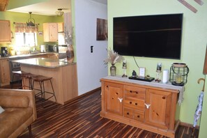 A kitchen with a central island, wooden cabinets, and a flat-screen TV mounted on the wall. - Incredible Whispering Pines Escape (Pinetop Country Club)