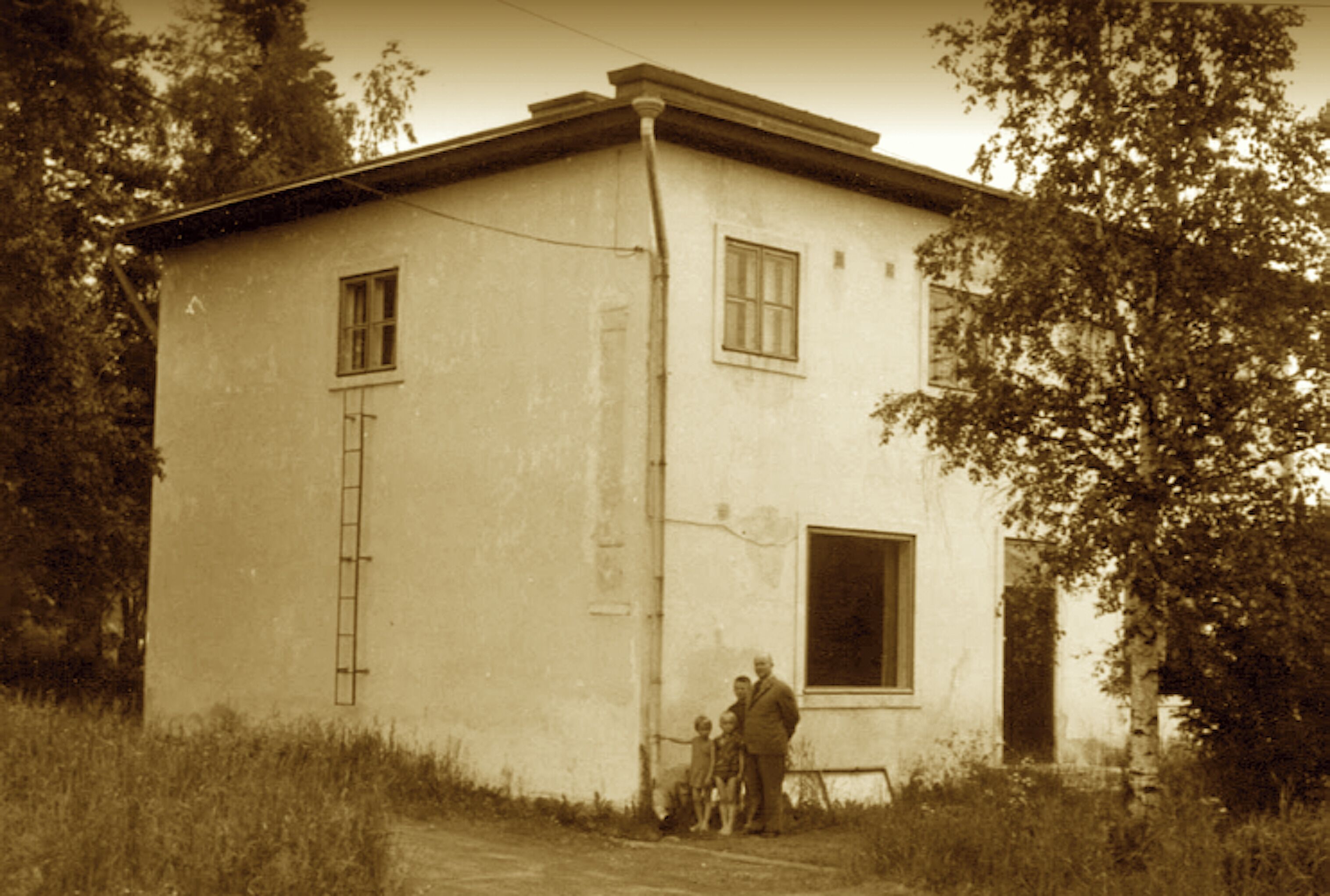 A two-story building with a simple, rectangular design, a visible window, and a door.