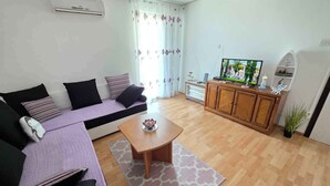 Ein Wohnzimmer mit einer Couch, einem Couchtisch, einem Fernseher auf einer Holzkommode und einer Topfpflanze.