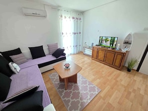 A living room with a sofa, a coffee table, a television on a wooden cabinet, and a potted plant. - Holiday apartment apartment with air conditioning and wifi (Klenovica)