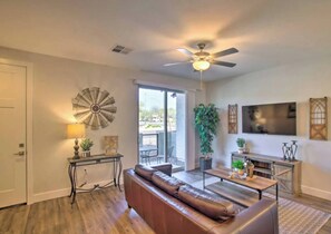 A living room with a brown leather sofa, a ceiling fan, a TV mounted on the wall, and a large window providing a view outside. - Modern Farmhouse Mesa Retreat (Mesa)
